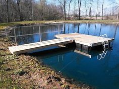 a dock sitting in the middle of a lake surrounded by grass and trees with no leaves on it