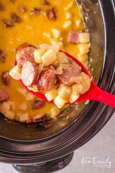 a spoon full of soup with sausage and potatoes in the crock pot, ready to be cooked