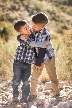 two young boys hugging each other while standing on rocks