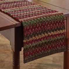 a wooden table topped with a red, green and brown placemat on top of a wooden table