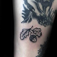 a black and white tattoo on the leg of a woman's arm with leaves and acorns