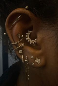 a woman's ear with gold piercings and dangling earrings on top of it