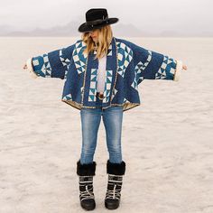 a woman standing in the desert wearing boots and a jacket with an argyle pattern on it