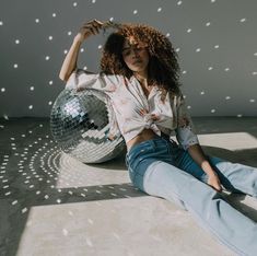 a woman sitting on the floor with her legs crossed and holding a disco ball in front of her