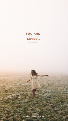 a woman in a white dress walking across a field with the words you are loved