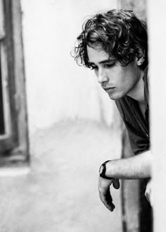 a young man leaning against a wall with his hand on the door handle and looking down