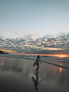 a person walking on the beach with a surfboard in their hand and sunset behind them