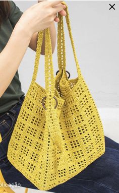 a woman is holding a yellow crocheted handbag in her lap and sitting down