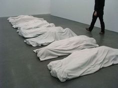 several white sheets are laying on the floor in an art gallery, with a person walking past them