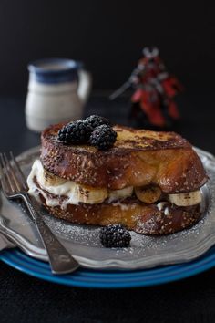 a stack of french toast topped with berries and whipped cream on a plate next to a fork