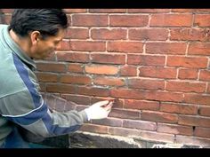 a man leaning against a brick wall with his hand on the ground and pointing at something