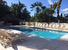 an empty swimming pool with lounge chairs around it and palm trees in the back ground