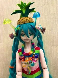 a doll with long blue hair wearing a pineapple hat and colorful necklaces on her head