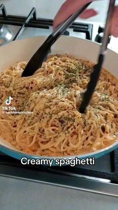 someone is stirring up some noodles in a pan on the stove with black tongs