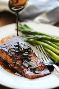 a piece of salmon on a plate with asparagus and sauce being drizzled over it