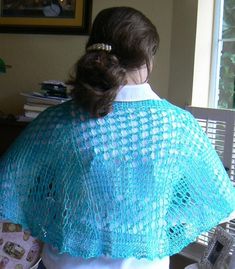 a woman wearing a blue crochet shawl sitting in front of a window