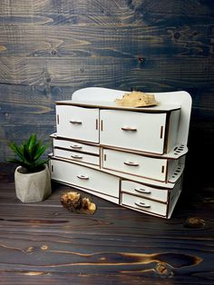 a white dresser with drawers next to a potted plant on top of wooden floor