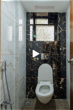 a white toilet sitting inside of a bathroom next to a walk in shower stall with black marble walls