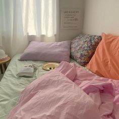 an unmade bed with pink sheets and pillows on it in front of a window