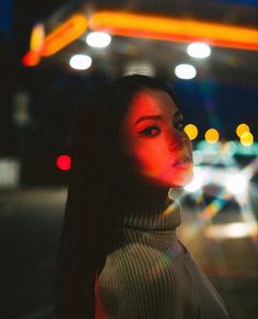 a woman standing in front of a gas station at night with her head turned to the side