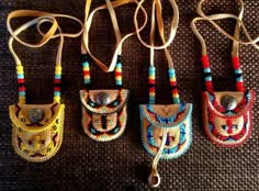 four colorful beaded purses are hanging on a brown cloth surface, one has a metal button and the other has a leather cord