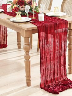 a red table runner on top of a wooden dining table with white plates and silverware