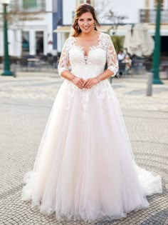 a woman in a white wedding dress standing on a cobblestone street smiling at the camera