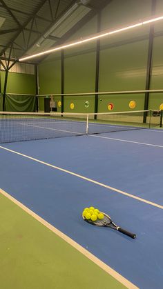 a tennis racket and ball on the ground in an indoor court with green walls