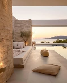 an outdoor living area with a pool and stone wall, candles on the floor and large windows overlooking the water