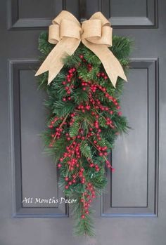 a christmas wreath on the front door with bows and berries hanging from it's side