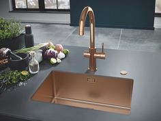 a kitchen sink with copper faucet and black counter top next to potted plants