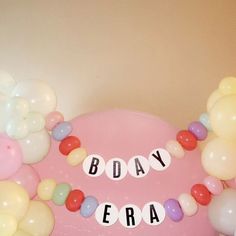 there is a pink cake with balloons around it and the words body era spelled in small letters