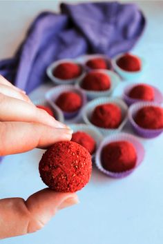 a hand holding a red ball in front of cupcakes