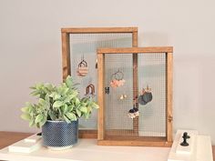 a wooden frame holds earrings and earring hooks on a white shelf next to a potted plant