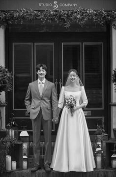 a bride and groom standing in front of a building with flowers on the porch, black and white photograph