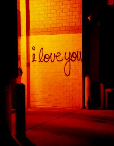 i love you written on the side of a brick building at night with red light