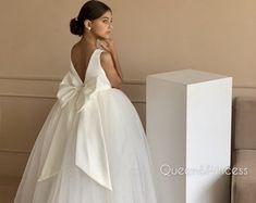 a woman in a white wedding dress standing next to a box and looking off into the distance