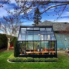 a small greenhouse in the middle of a yard with potted plants and flowers inside