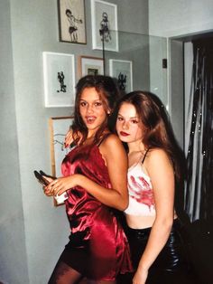 two young women standing next to each other in front of a wall with pictures on it