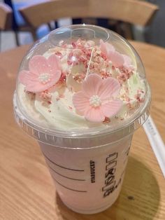 a plastic cup filled with white frosting and pink flowers on top of a wooden table