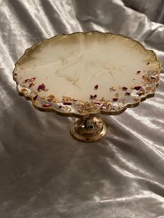 a white and gold platter with flowers on it sitting on a silver satin surface