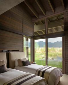 two beds in a room with wooden walls and floor to ceiling windows overlooking the mountains