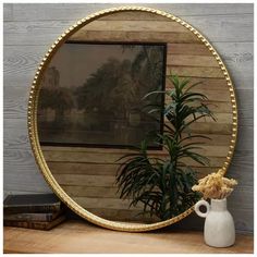 a round mirror sitting on top of a wooden table next to a potted plant