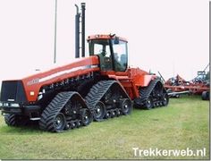 an orange tractor parked on top of a lush green field next to other farm equipment