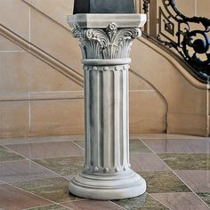 a white pillar on the ground in front of a stair case with a clock above it