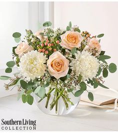 a vase filled with white flowers and greenery on top of a table next to an open book