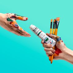 two hands are holding paintbrushes and one has their fingers painted with different colors