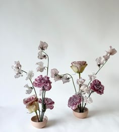 two vases with flowers in them on a white surface, one is pink and the other is purple