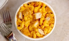 a white bowl filled with macaroni and cheese on top of a table next to a fork