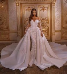 a woman standing in front of a door wearing a wedding dress with long sleeves and high slit